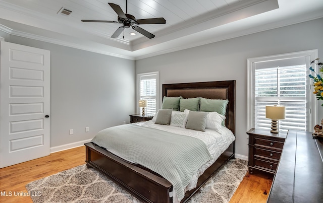 bedroom with crown molding, light hardwood / wood-style flooring, and a raised ceiling