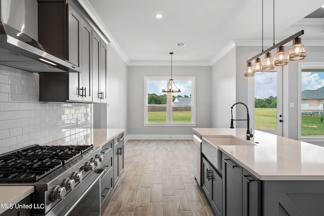 kitchen featuring a wealth of natural light, an island with sink, wall chimney range hood, and gray cabinetry