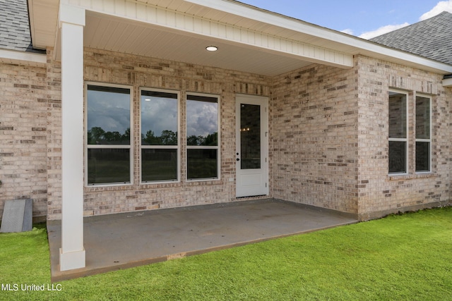 view of exterior entry with a patio area and a lawn