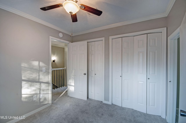 unfurnished bedroom featuring multiple closets, crown molding, a textured ceiling, carpet floors, and ceiling fan