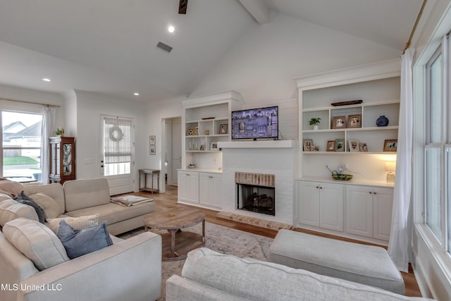 living room with beam ceiling, light hardwood / wood-style flooring, high vaulted ceiling, and a brick fireplace