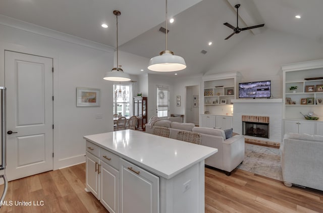 kitchen with decorative light fixtures, white cabinetry, a center island, and light hardwood / wood-style flooring