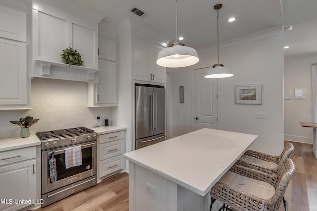 kitchen featuring appliances with stainless steel finishes, hanging light fixtures, light hardwood / wood-style floors, a kitchen island, and white cabinetry