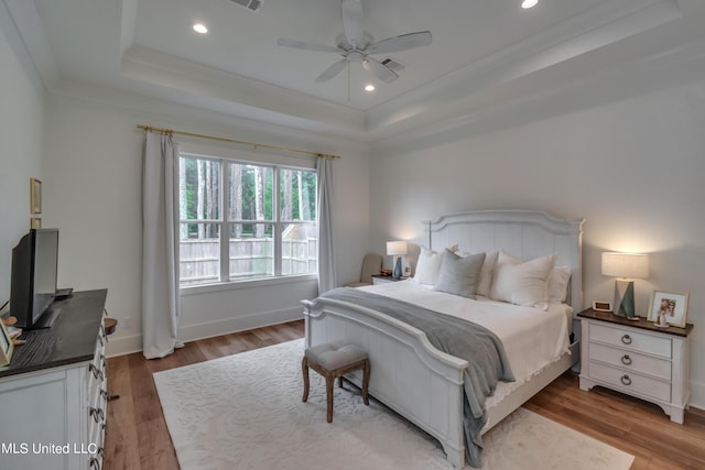 bedroom featuring a raised ceiling, light hardwood / wood-style floors, crown molding, and ceiling fan