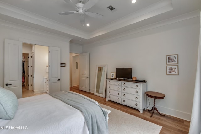 bedroom with light hardwood / wood-style flooring, a tray ceiling, ornamental molding, ceiling fan, and ensuite bathroom