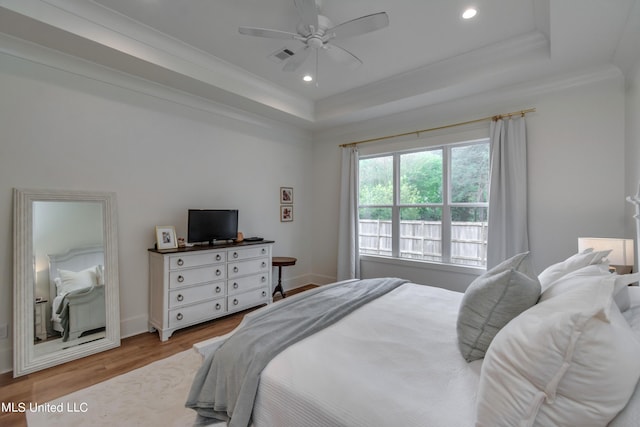 bedroom with ceiling fan, ornamental molding, light hardwood / wood-style floors, and a raised ceiling