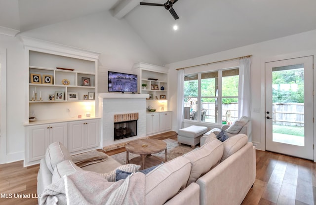 living room featuring beam ceiling, high vaulted ceiling, light hardwood / wood-style floors, and a brick fireplace