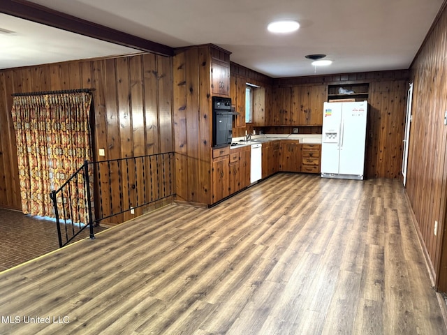 kitchen with wooden walls, white appliances, a sink, wood finished floors, and beam ceiling