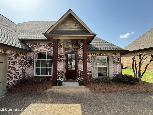 entrance to property with brick siding and a shingled roof