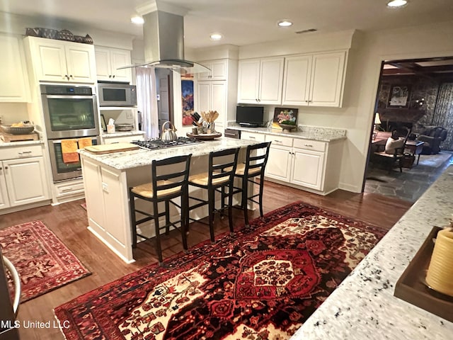 kitchen featuring island exhaust hood, stainless steel appliances, white cabinets, and light stone counters