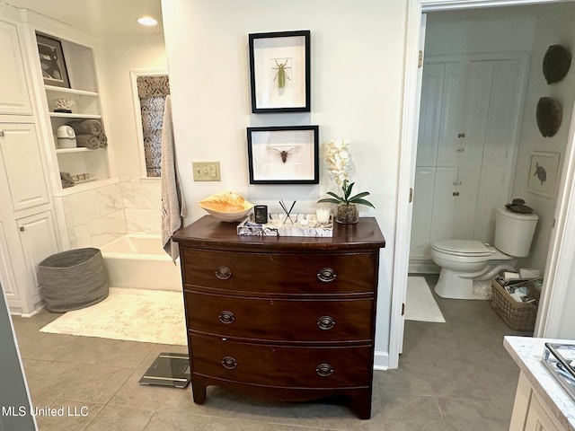 bathroom featuring tile patterned flooring, vanity, a tub to relax in, toilet, and built in features