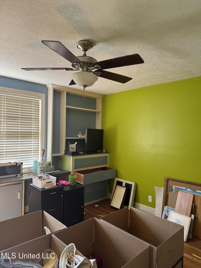 home office with a ceiling fan, dark wood-style flooring, and a textured ceiling