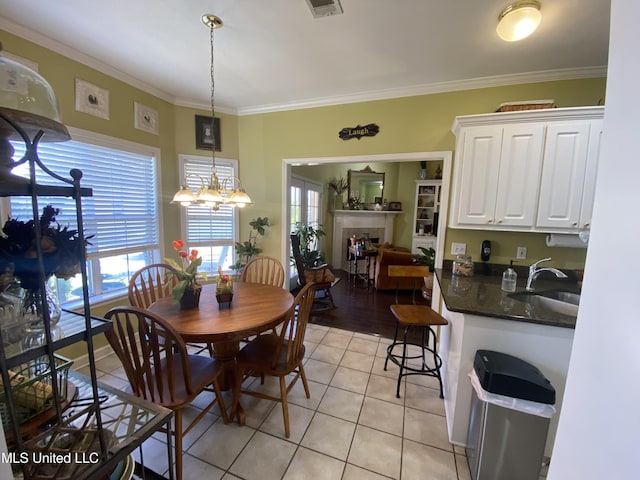 dining room with light tile patterned flooring, visible vents, a tiled fireplace, and crown molding