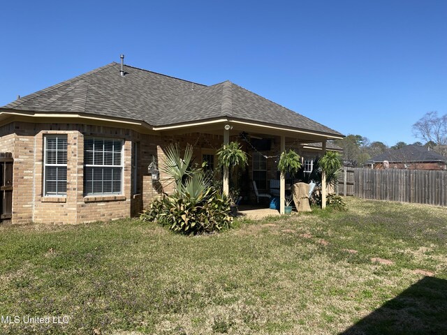 rear view of house with a yard, brick siding, ceiling fan, and fence