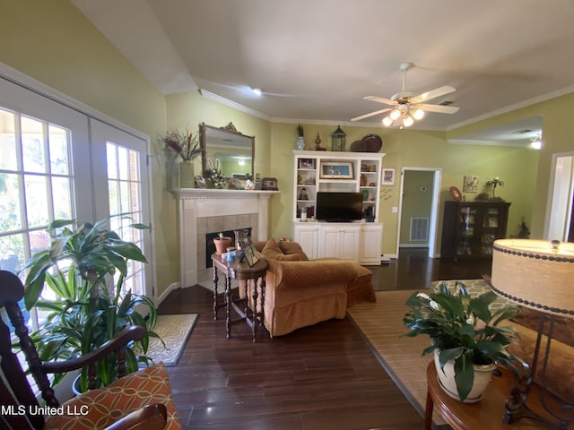 living room with visible vents, ornamental molding, a tiled fireplace, dark wood-style floors, and ceiling fan