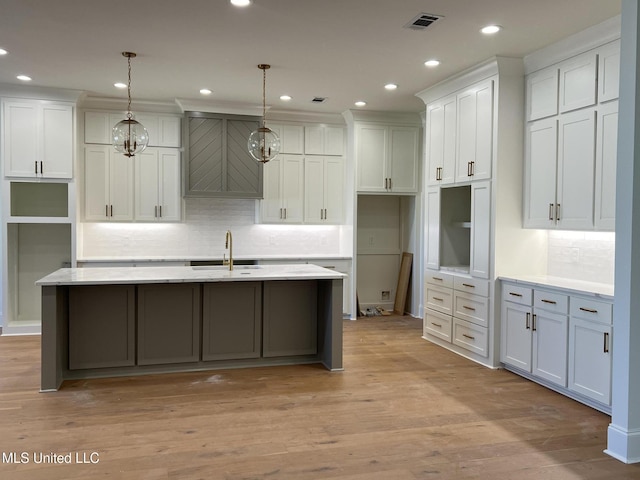 kitchen with decorative light fixtures, white cabinets, an island with sink, and light hardwood / wood-style flooring