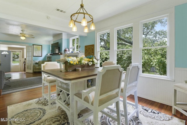 dining space with hardwood / wood-style floors, ceiling fan with notable chandelier, and a healthy amount of sunlight