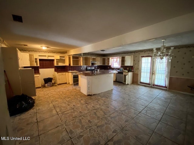 kitchen with wallpapered walls, stone tile floors, dark countertops, a kitchen island with sink, and stainless steel appliances