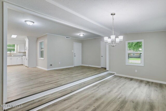 unfurnished room with sink, a notable chandelier, light wood-type flooring, and plenty of natural light