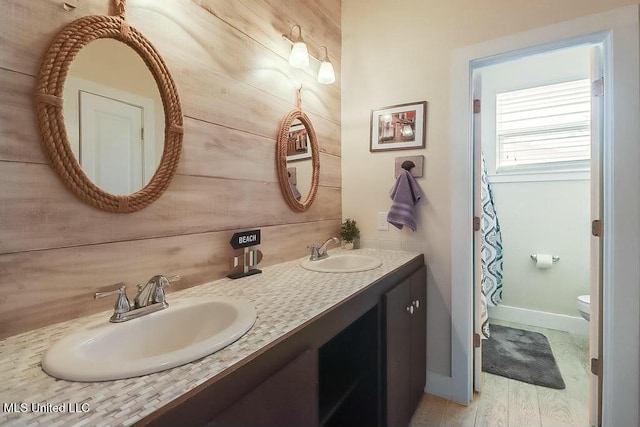 full bath with a sink, wood walls, and toilet