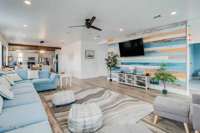 living room with visible vents, a ceiling fan, an accent wall, wood finished floors, and recessed lighting