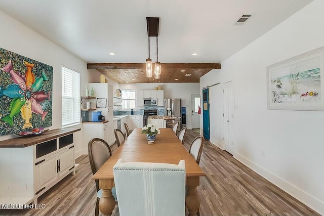 dining room featuring baseboards, visible vents, beam ceiling, and wood finished floors