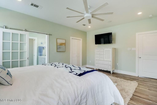 bedroom with a barn door, wood finished floors, visible vents, and recessed lighting