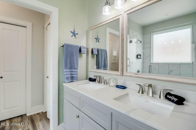 bathroom with double vanity, a tile shower, a sink, and wood finished floors