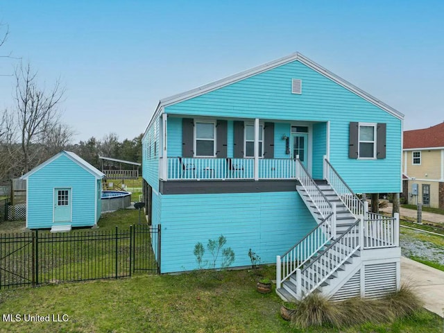 coastal home with covered porch, a front yard, fence, an outdoor structure, and stairs