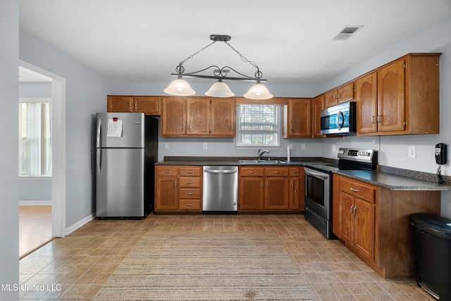 kitchen with brown cabinets, dark countertops, visible vents, appliances with stainless steel finishes, and a sink