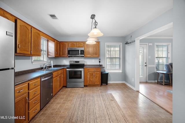 kitchen with brown cabinets, stainless steel appliances, dark countertops, hanging light fixtures, and a sink