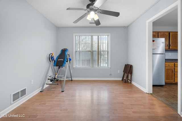 exercise room featuring light wood finished floors, baseboards, visible vents, and a ceiling fan