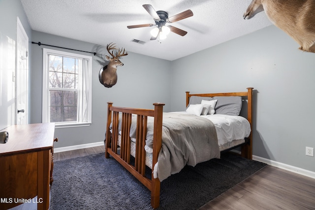 bedroom with a textured ceiling, wood finished floors, visible vents, and baseboards