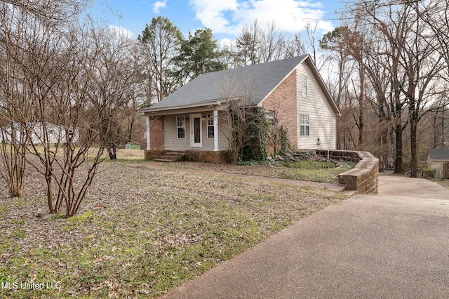 view of front of home with driveway, covered porch, a shingled roof, and brick siding