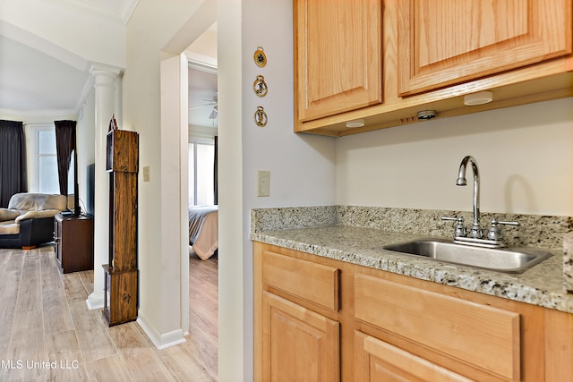 kitchen featuring light stone counters, ornamental molding, light brown cabinetry, sink, and light hardwood / wood-style floors