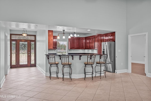 kitchen with a kitchen bar, stainless steel refrigerator with ice dispenser, light tile patterned floors, and pendant lighting