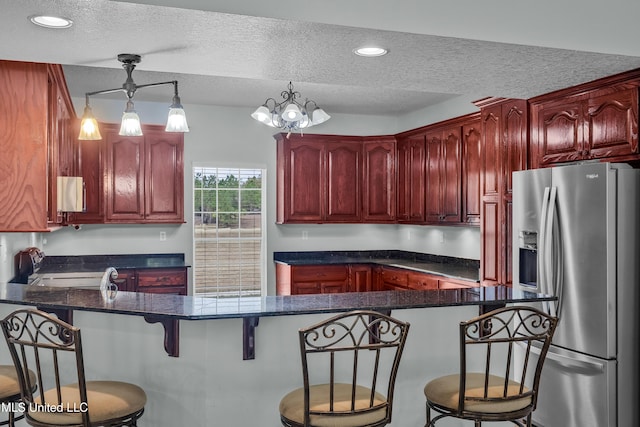 kitchen with kitchen peninsula, stainless steel fridge, a textured ceiling, an inviting chandelier, and hanging light fixtures