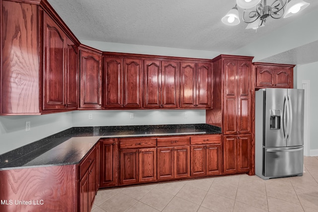 kitchen with dark stone countertops, stainless steel fridge, a chandelier, a textured ceiling, and light tile patterned floors