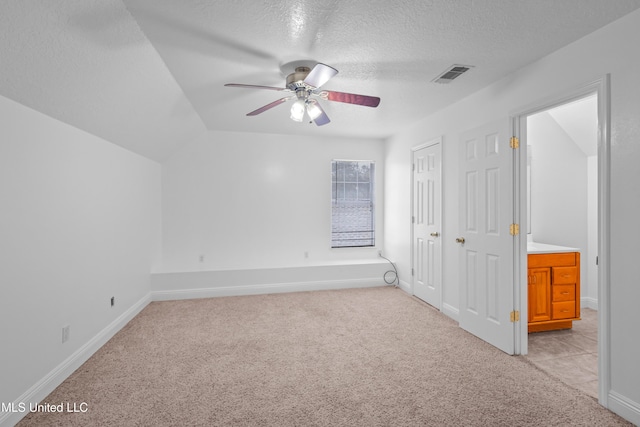 unfurnished bedroom featuring ceiling fan, ensuite bathroom, lofted ceiling, a textured ceiling, and light carpet