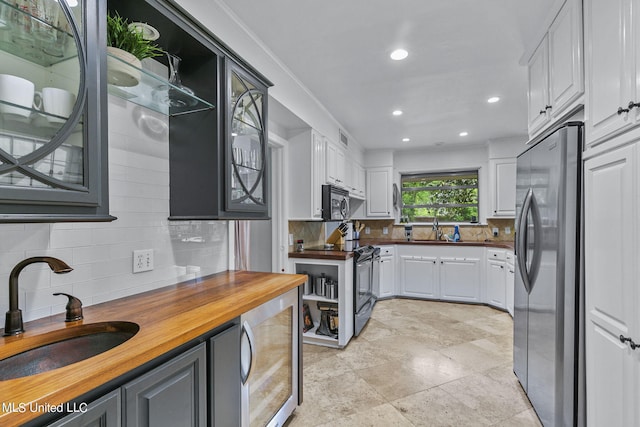 kitchen with white cabinetry, butcher block counters, sink, and stainless steel refrigerator