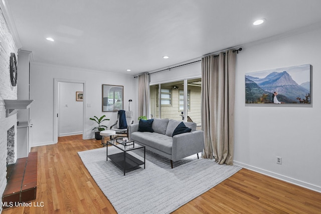 living room with ornamental molding, light wood-type flooring, and a brick fireplace