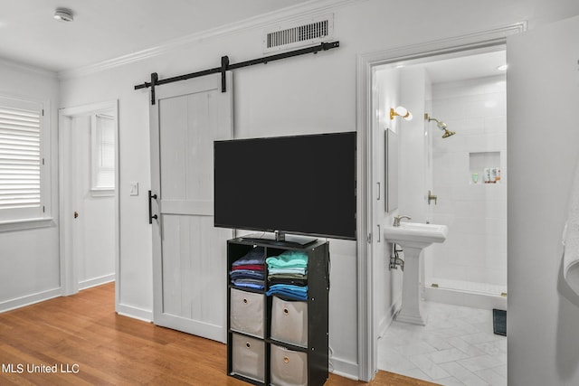 bedroom with ensuite bath, crown molding, light wood-type flooring, and a barn door