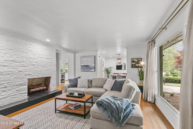 living room featuring a stone fireplace, light hardwood / wood-style flooring, ornamental molding, and a healthy amount of sunlight