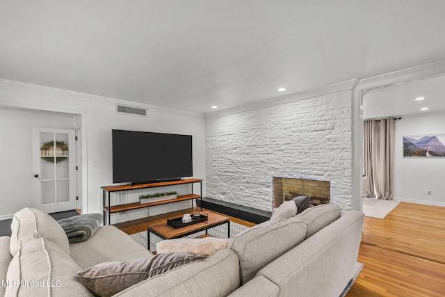 living room with a stone fireplace, crown molding, and hardwood / wood-style floors