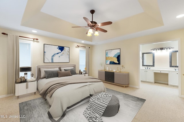 bedroom featuring light colored carpet, baseboards, a raised ceiling, and connected bathroom