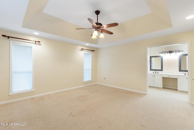 unfurnished bedroom with a tray ceiling, recessed lighting, light colored carpet, and baseboards