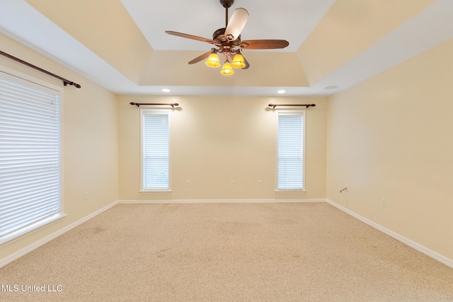 unfurnished room with a raised ceiling, carpet flooring, baseboards, and ceiling fan