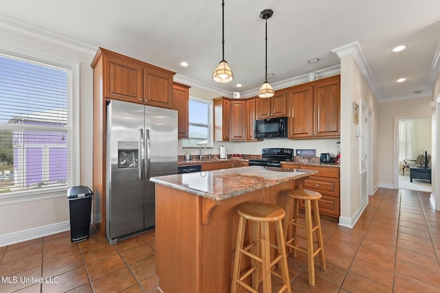 kitchen featuring a center island, black appliances, a kitchen bar, a wealth of natural light, and light stone countertops