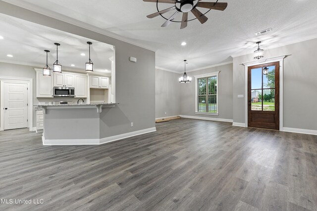 unfurnished living room with ceiling fan with notable chandelier, ornamental molding, dark hardwood / wood-style floors, and a textured ceiling