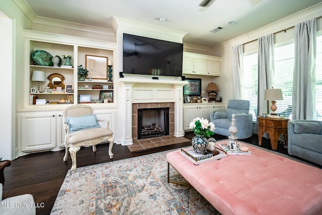 living room with built in shelves, ornamental molding, a tile fireplace, and dark hardwood / wood-style floors